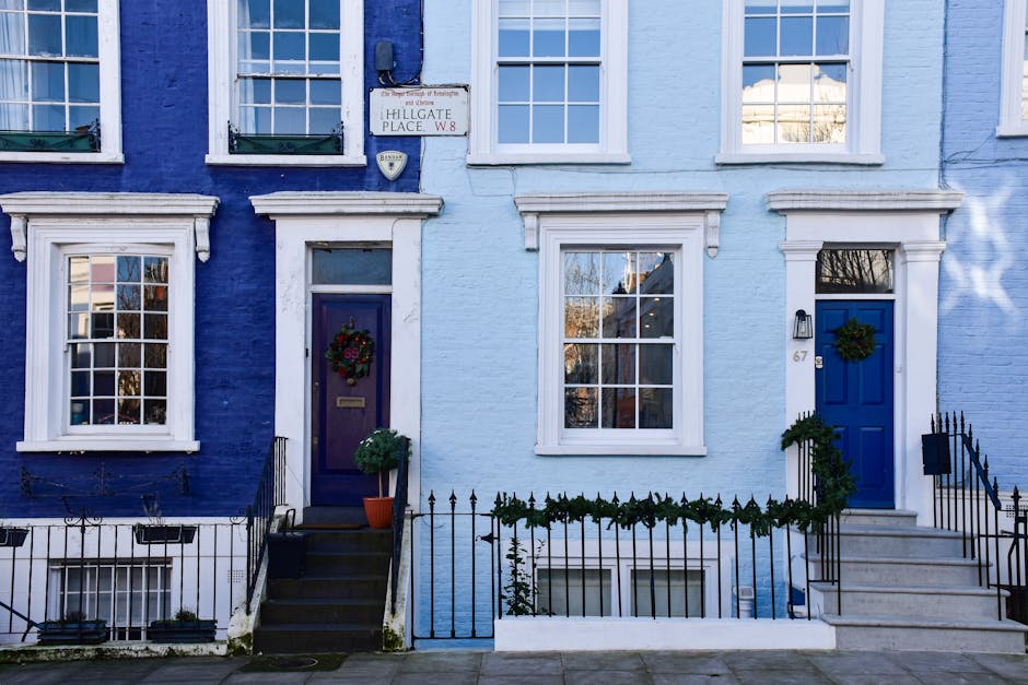 A row of two-storey terraced houses with light blue and dark blue facades, each featuring white-framed sash windows and front doors, one of which is decorated with a festive wreath. Black wrought-iron